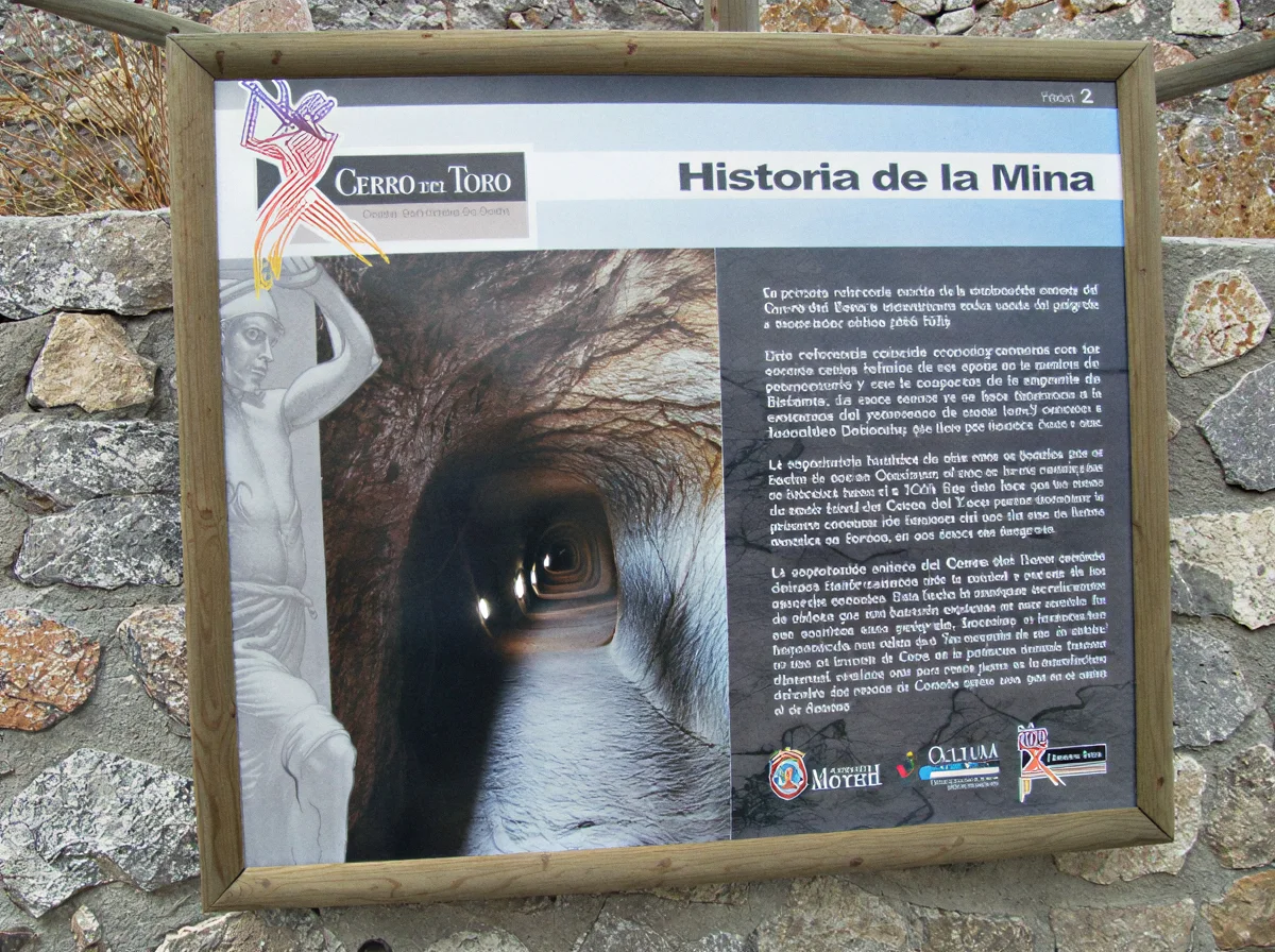 Panel interpretativo sobre la historia de la mina junto a una entrada excavada en la roca