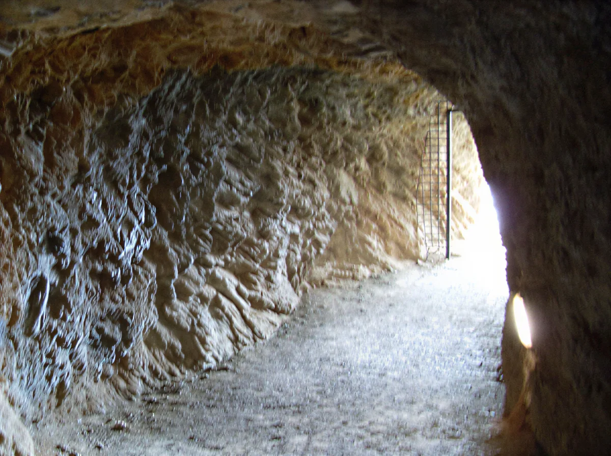 Tramo de galería excavado en la roca con salida iluminada